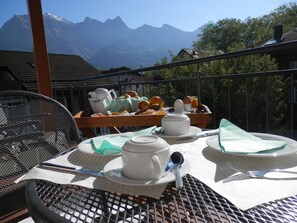 A breakfast setup on a balcony with a mountain view, including a tray with eggs, toast, and fruit.