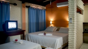 A hotel room with two beds, a desk with a computer, a brick accent wall, and a window with curtains. - Pousada California (Aracati)