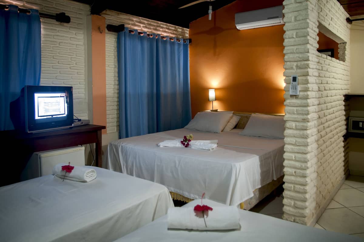 A hotel room with two beds, a desk with a computer, a brick accent wall, and a window with curtains.