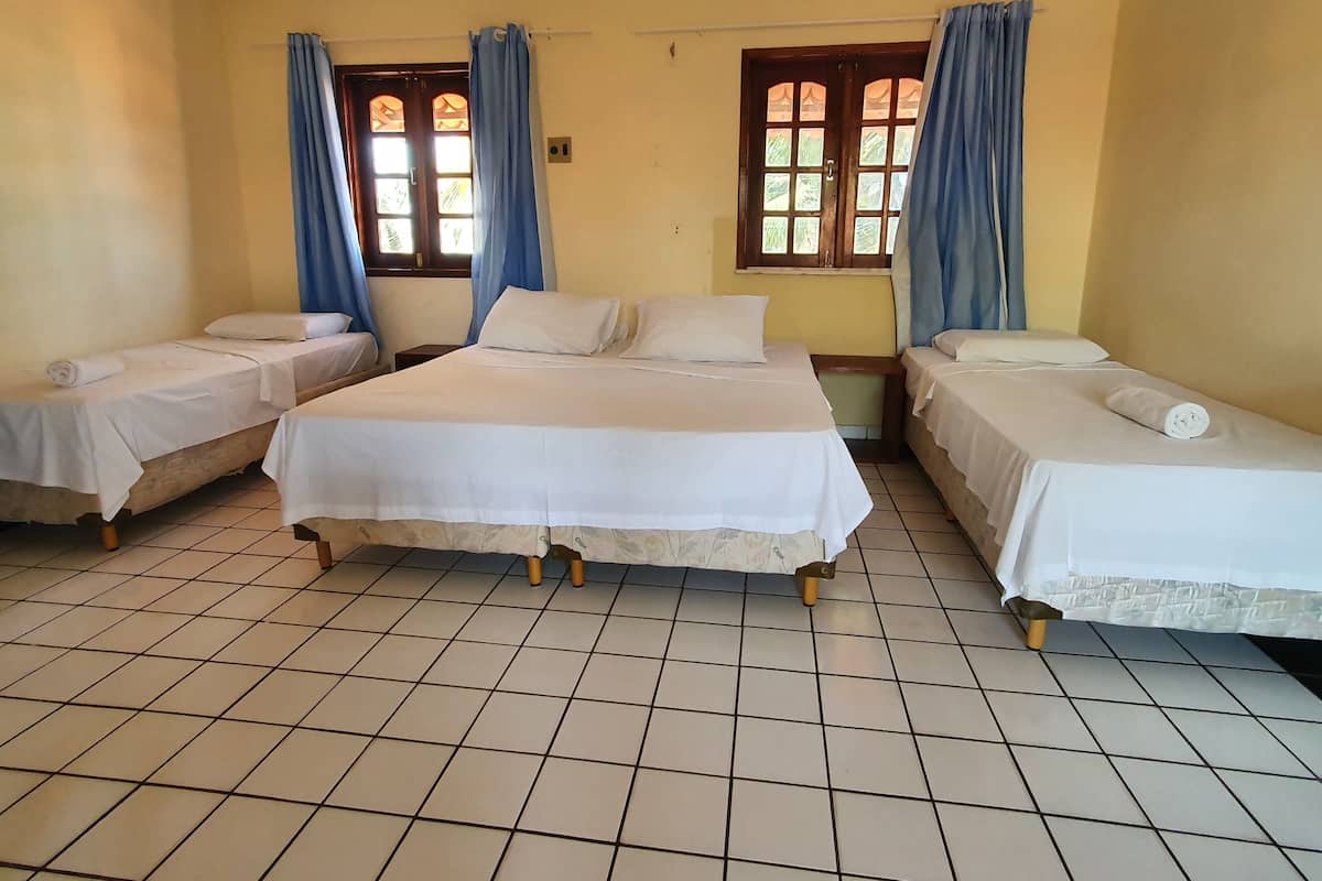 A room with three single beds, a large bed, and a window with curtains.