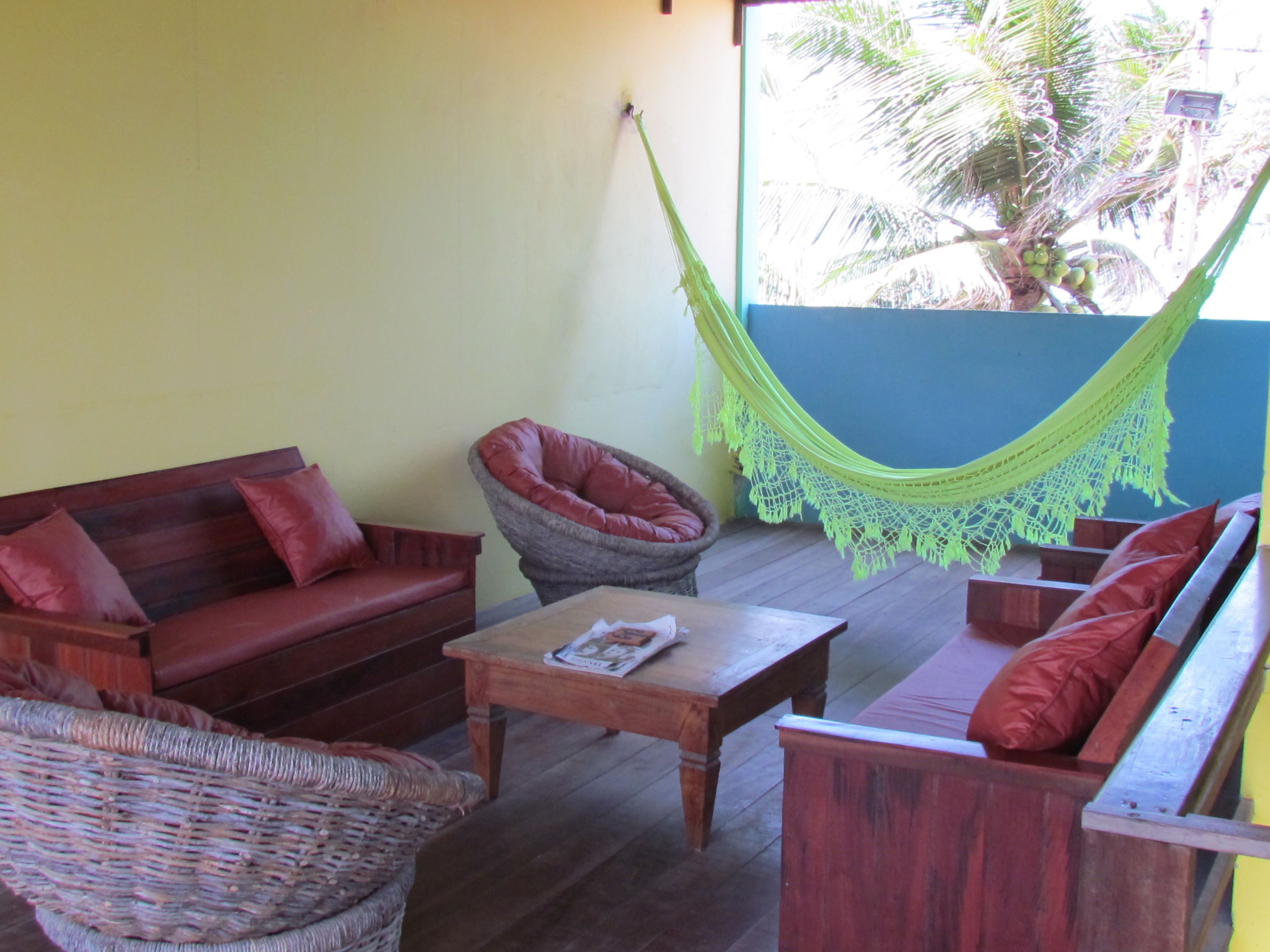 Un rincón acogedor con una hamaca, un sofá de madera y un sillón de mimbre.