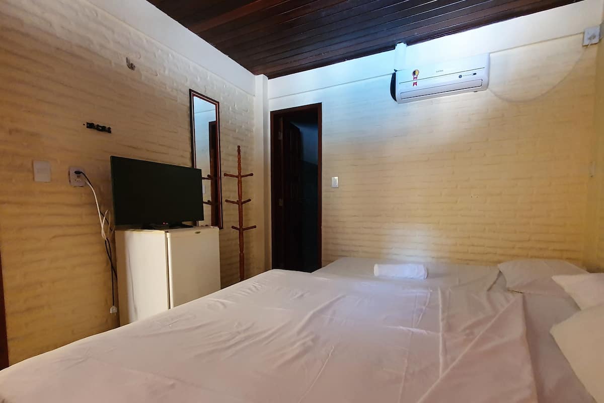 A room with a bed, a television on a stand, a heater, and a door.