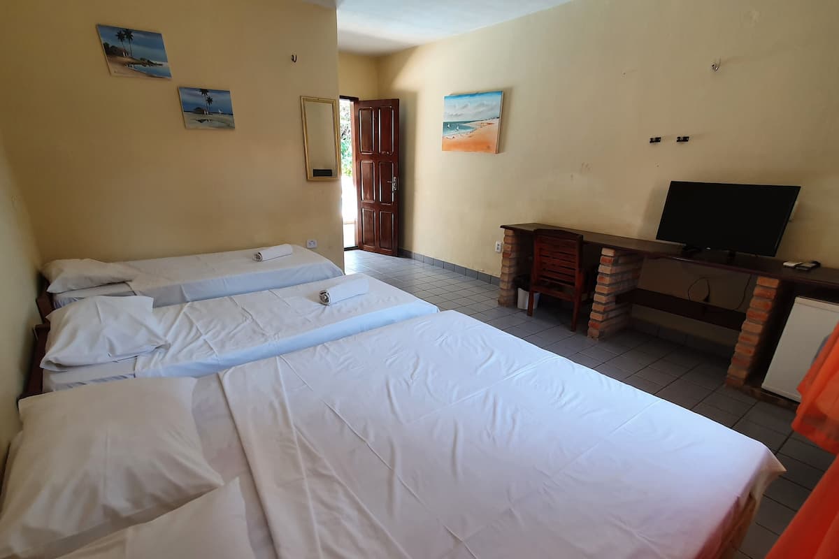 A hotel room with three beds, a desk with a television, and a door leading outside.