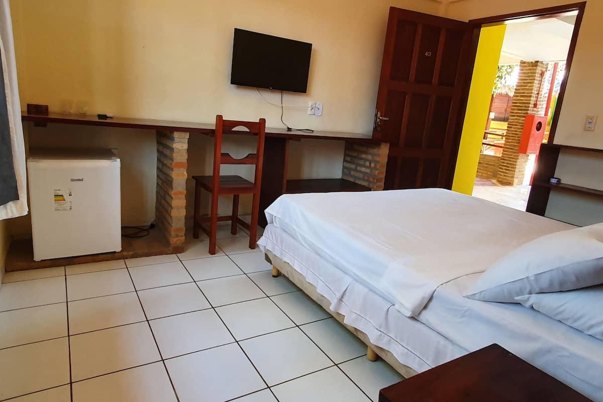 A hotel room with a bed, a desk with a chair, a television, and a refrigerator.