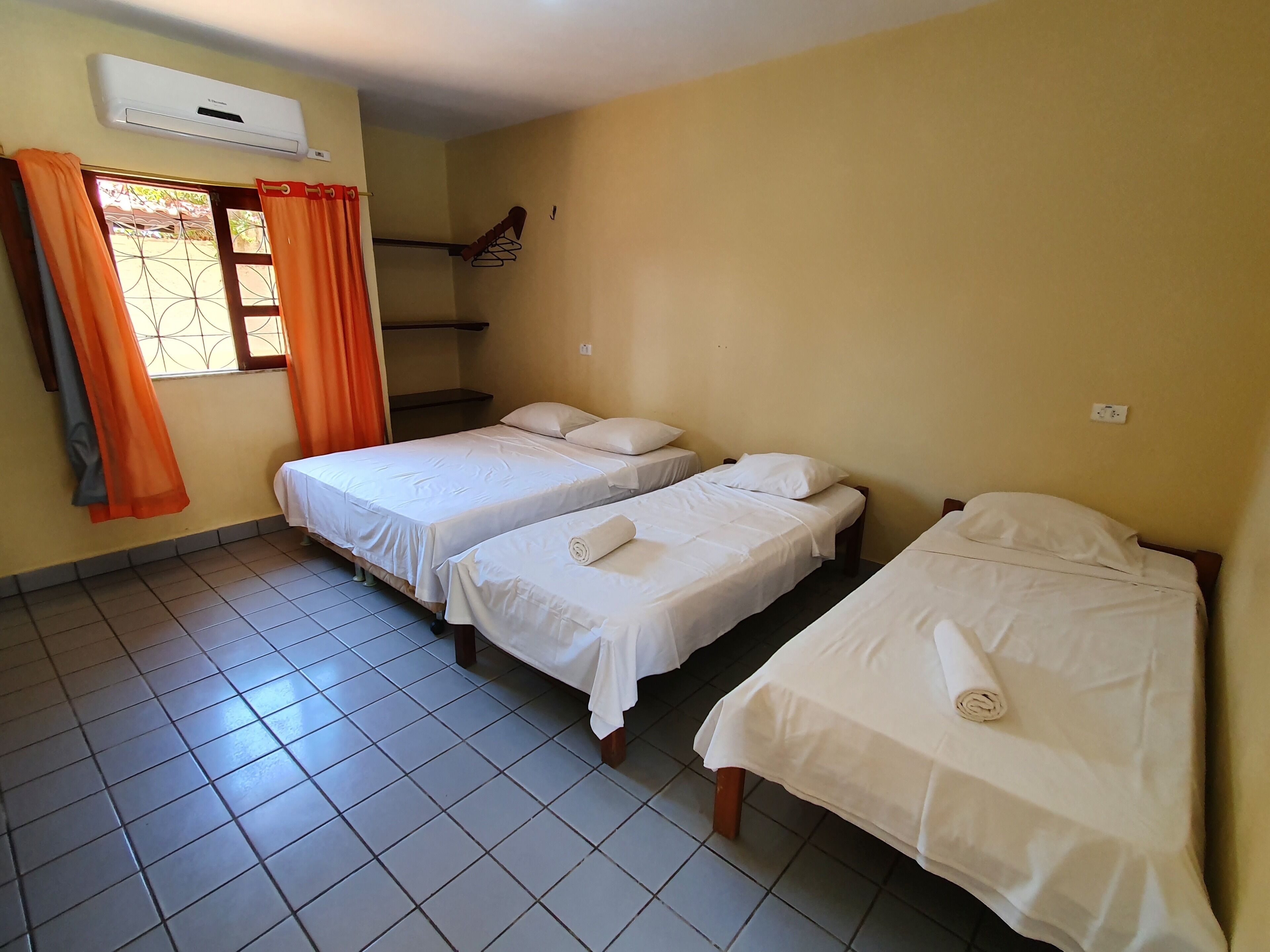 A room with two beds, an air conditioning unit, a window with curtains, and a tiled floor.