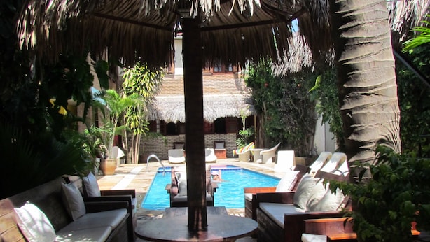 A pool area with lounge chairs and a thatched roof structure. - Pousada California (Aracati)