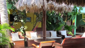 A tropical outdoor seating area with wooden furniture and a thatched roof. - Pousada California (Aracati)