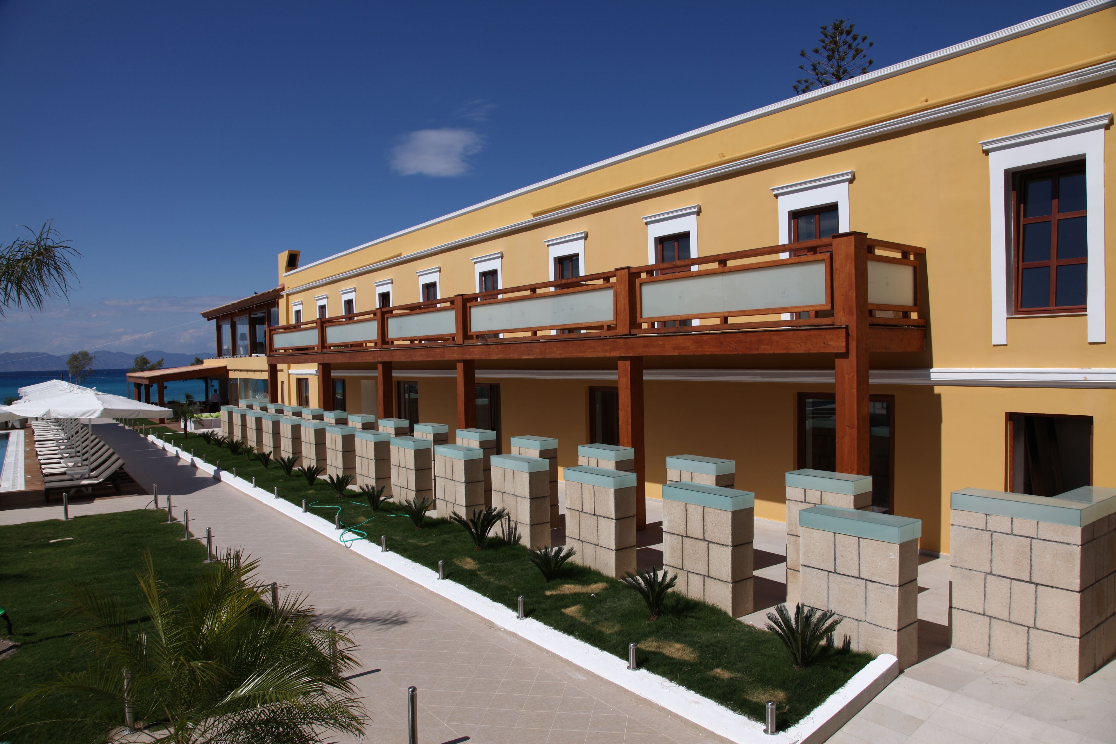 A hotel with a yellow facade, a covered outdoor area with seating, and a view of the sea.