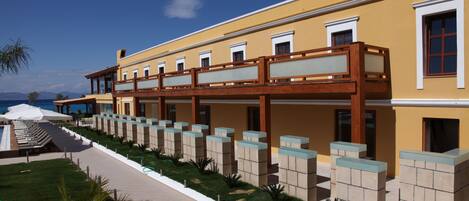A hotel with a yellow facade, a covered outdoor area with seating, and a view of the sea.