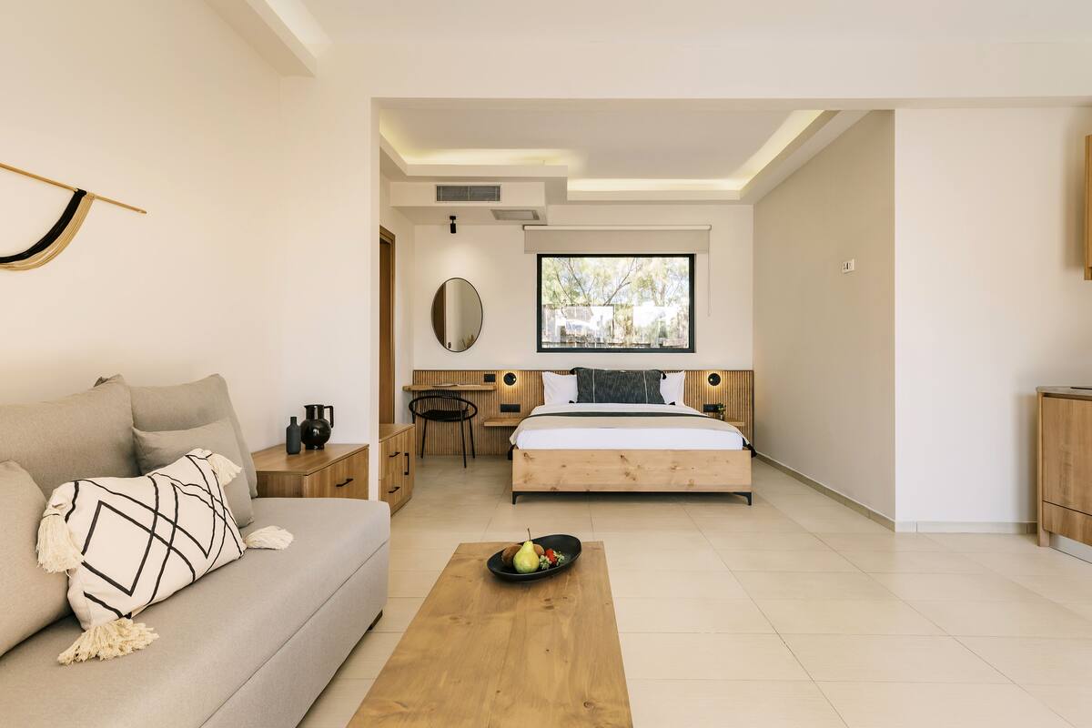 Un dormitorio moderno con cama, sofá, mesita de noche de madera, escritorio y ventana.