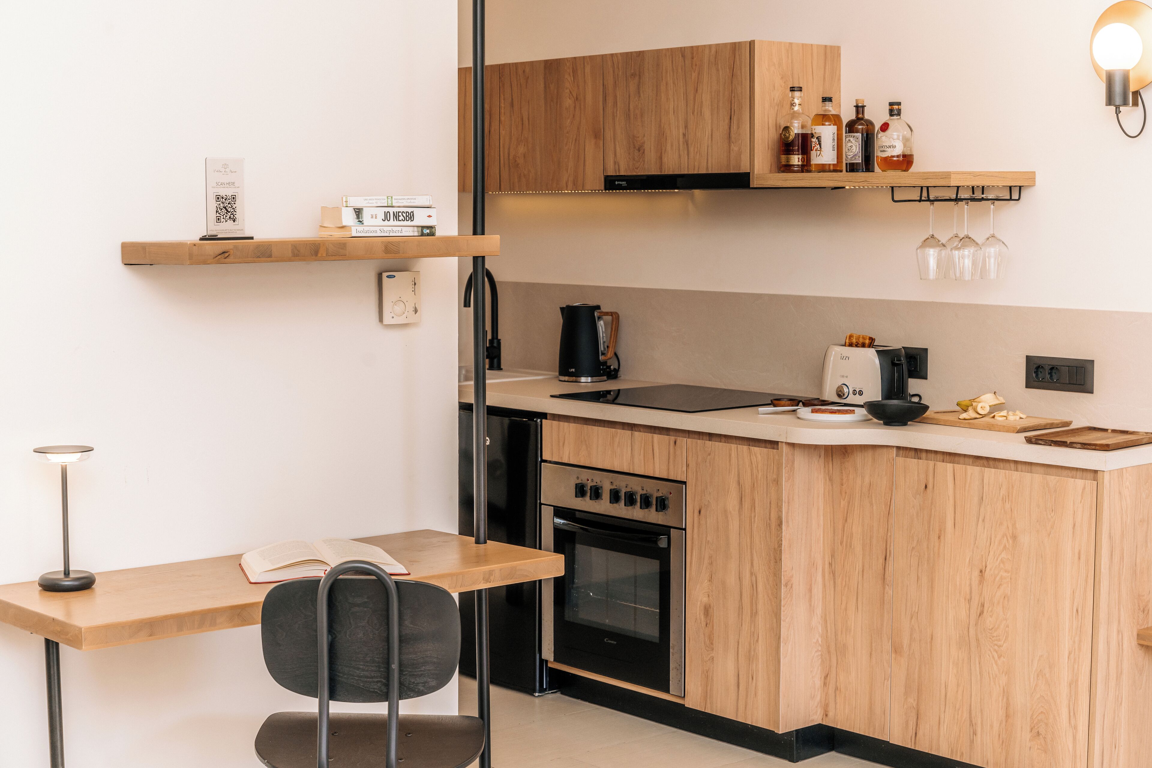 A modern kitchen with wooden cabinets, a built-in oven, a coffee maker, and a small dining area with a table and chair.