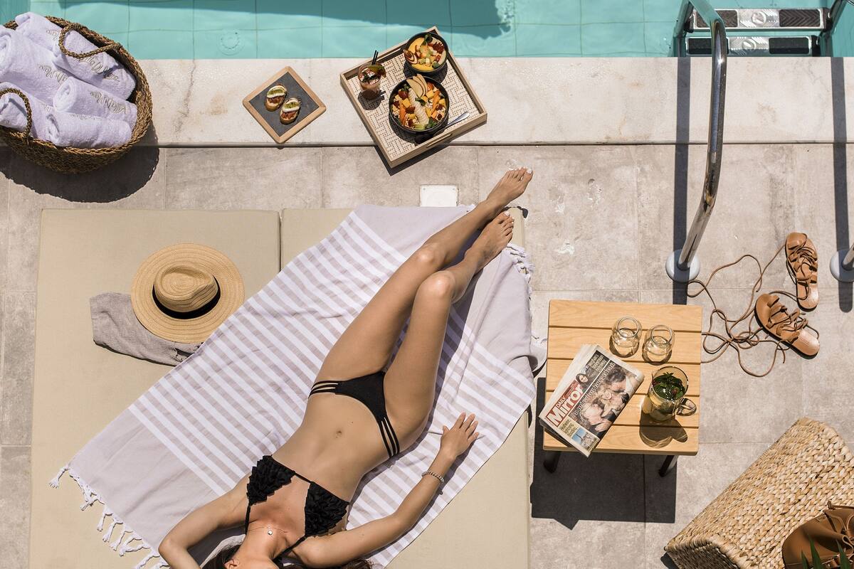 Un área de piscina con una silla de descanso, una toalla, una mesa con comida y bebidas, y un flotador amarillo.