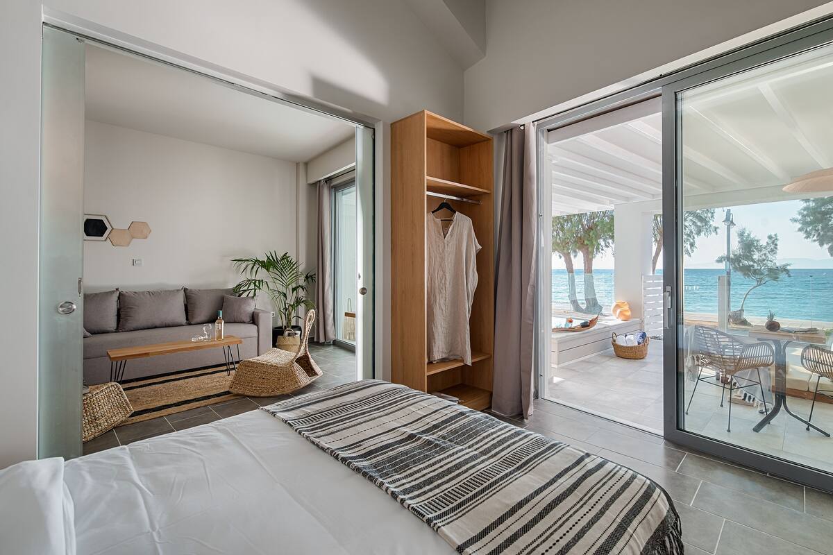 Un dormitorio moderno con una cama grande, un armario de madera, un sofá y vistas al mar a través de un ventanal corredero.
