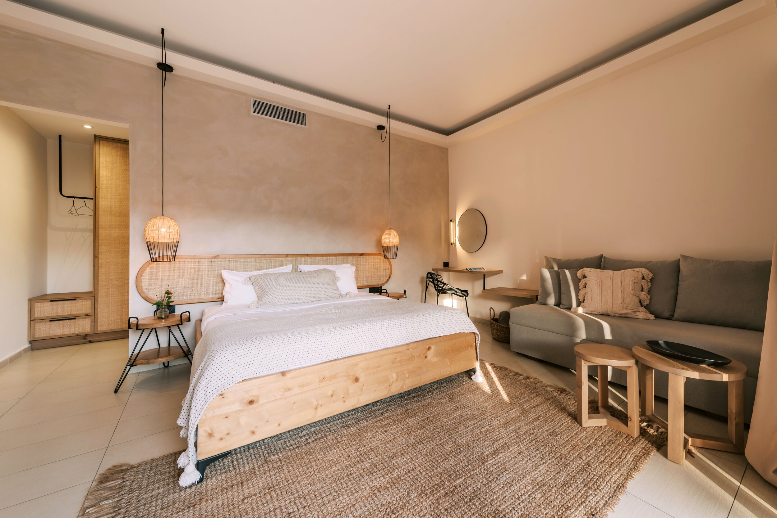 Une chambre à coucher moderne avec un lit en bois, un canapé gris, une petite table et un luminaire suspendu.