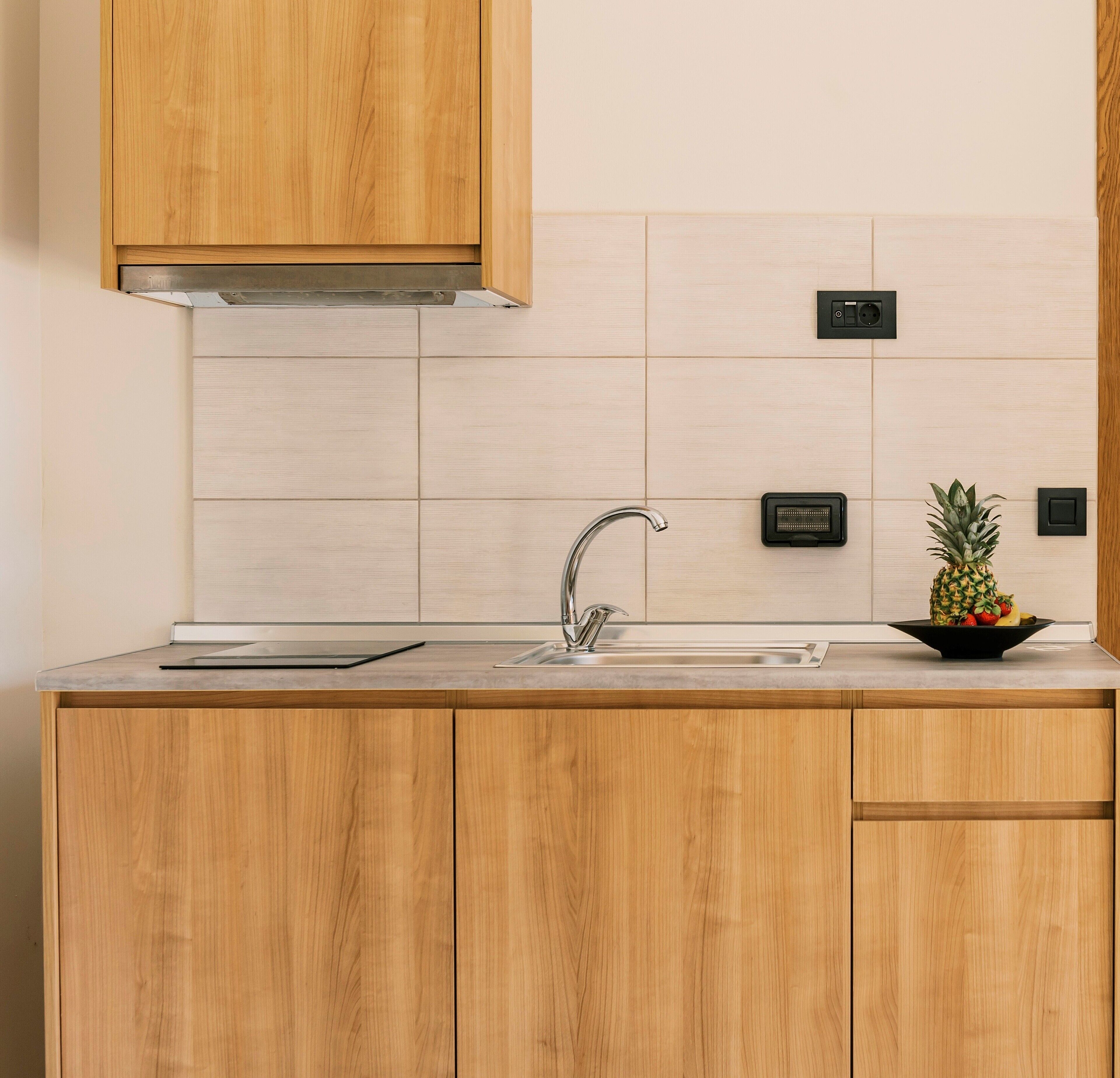 Una cocina moderna con armarios de madera, un lavamanos de acero inoxidable y una campana extractora integrada.