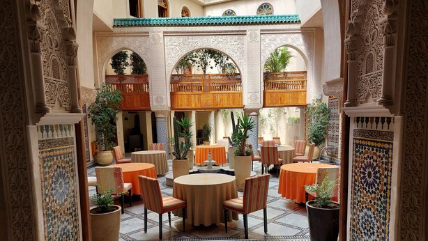 An interior courtyard with ornate arches, tiled flooring, and round tables with chairs. - Riad Andalib (Fes)