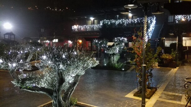 Un espacio exterior nocturno con luces decorativas, una escalera y un edificio con ventanas iluminadas.