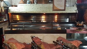 Un área de cocina con salpicadero de ladrillo, encimera blanca y una estufa grande. Hay vajilla de cerámica y un certificado enmarcado en la pared.