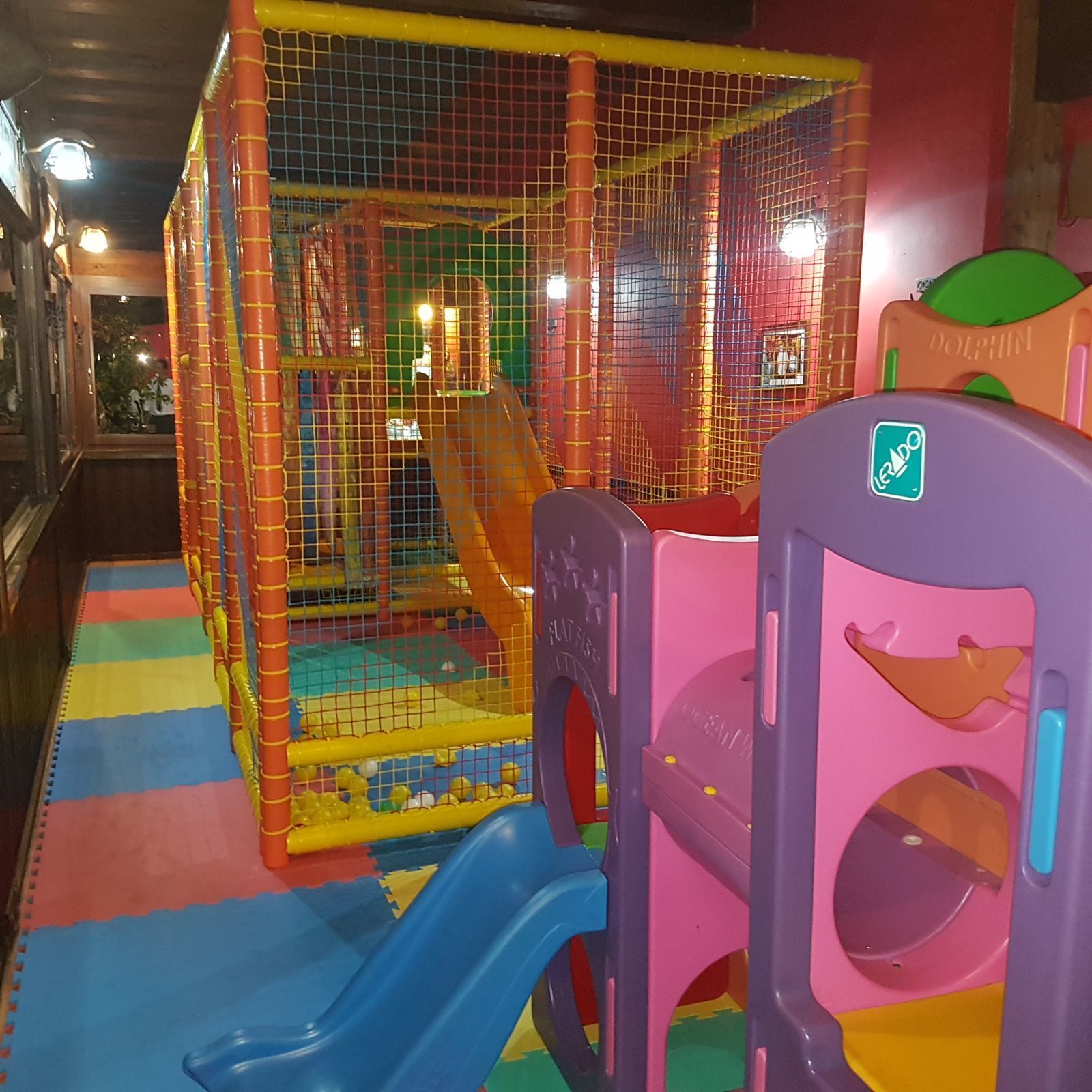 Ein Spielbereich für Kinder mit Rutsche und Bällebad, umgeben von einem Sicherheitsnetz.