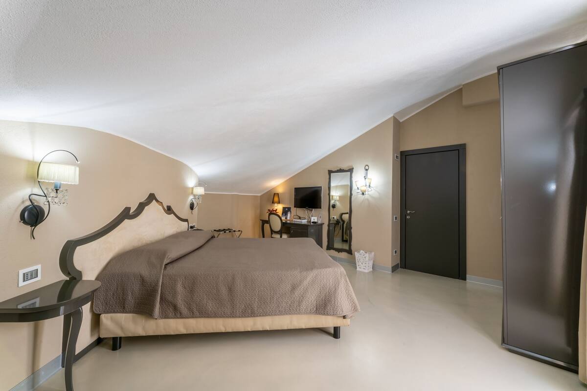 Un dormitorio con cama, mesita de noche, lámpara, televisor, escritorio, espejo y armario.