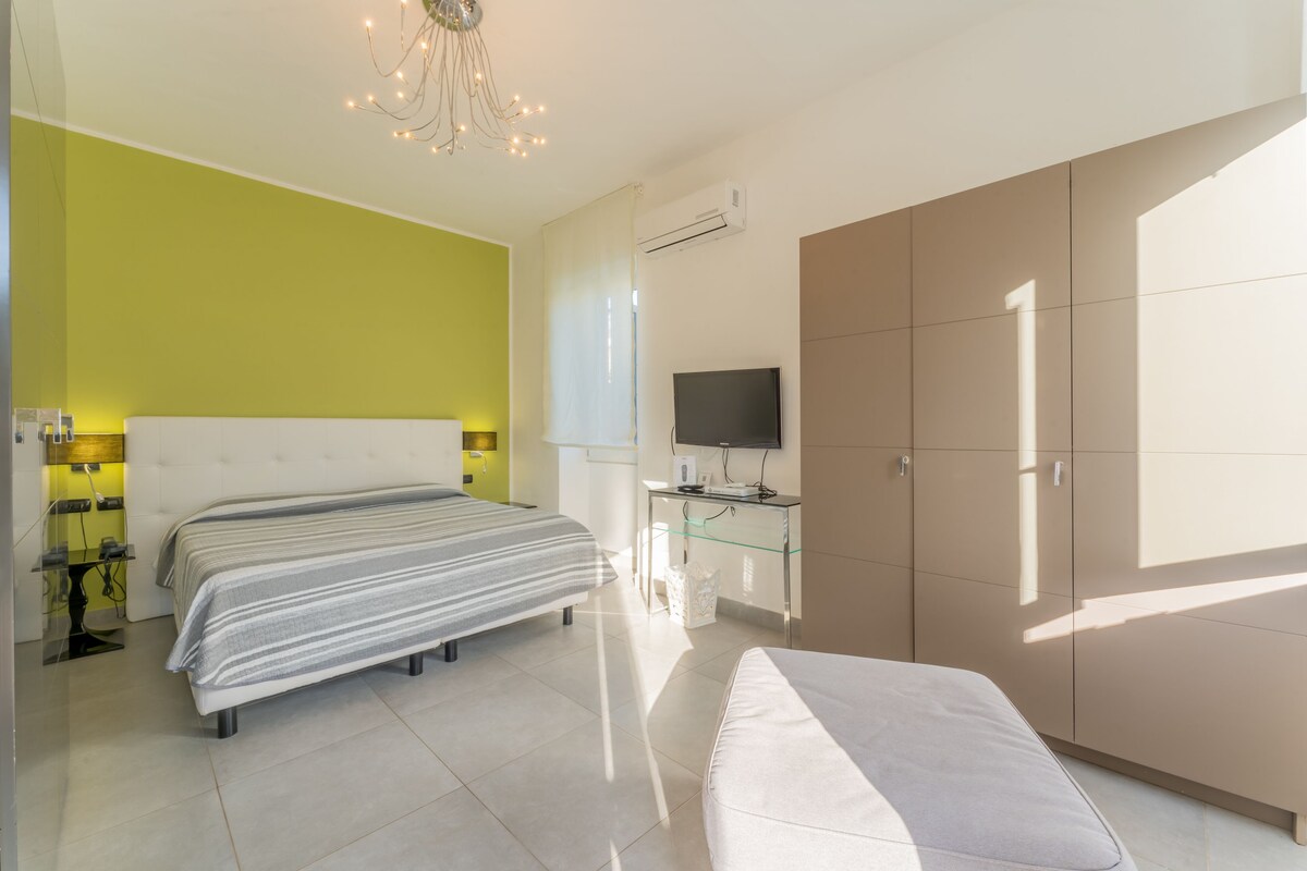 A modern bedroom with a large bed, a bedside table, a TV, and a wardrobe.