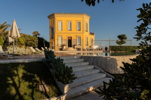 A yellow building with a pool, surrounded by steps and greenery. - Villa Mosca (Alghero)