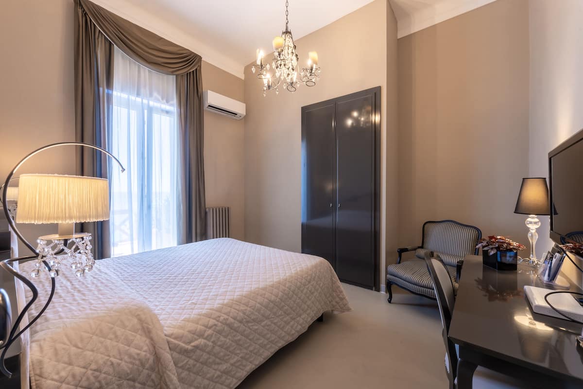 Una habitación de hotel con una cama grande, un escritorio con silla, una araña y un armario.