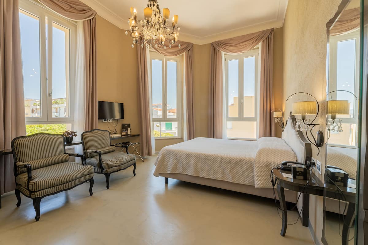 Habitación de hotel con una cama grande, dos sillones, un televisor y un escritorio con lámpara.