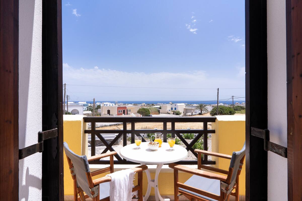 Un balcón con mesa y sillas, con vistas a una zona costera con edificios y cielo despejado.
