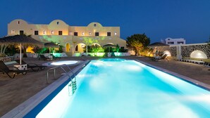 Una piscina con sillones de descanso y un edificio al fondo con ventanas de arco y pared de piedra.