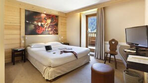 A hotel room with a large bed, a desk with a computer, a chair, and a television.