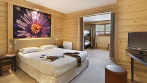 A hotel room with a large bed, a TV, a desk, and a door leading to another room.