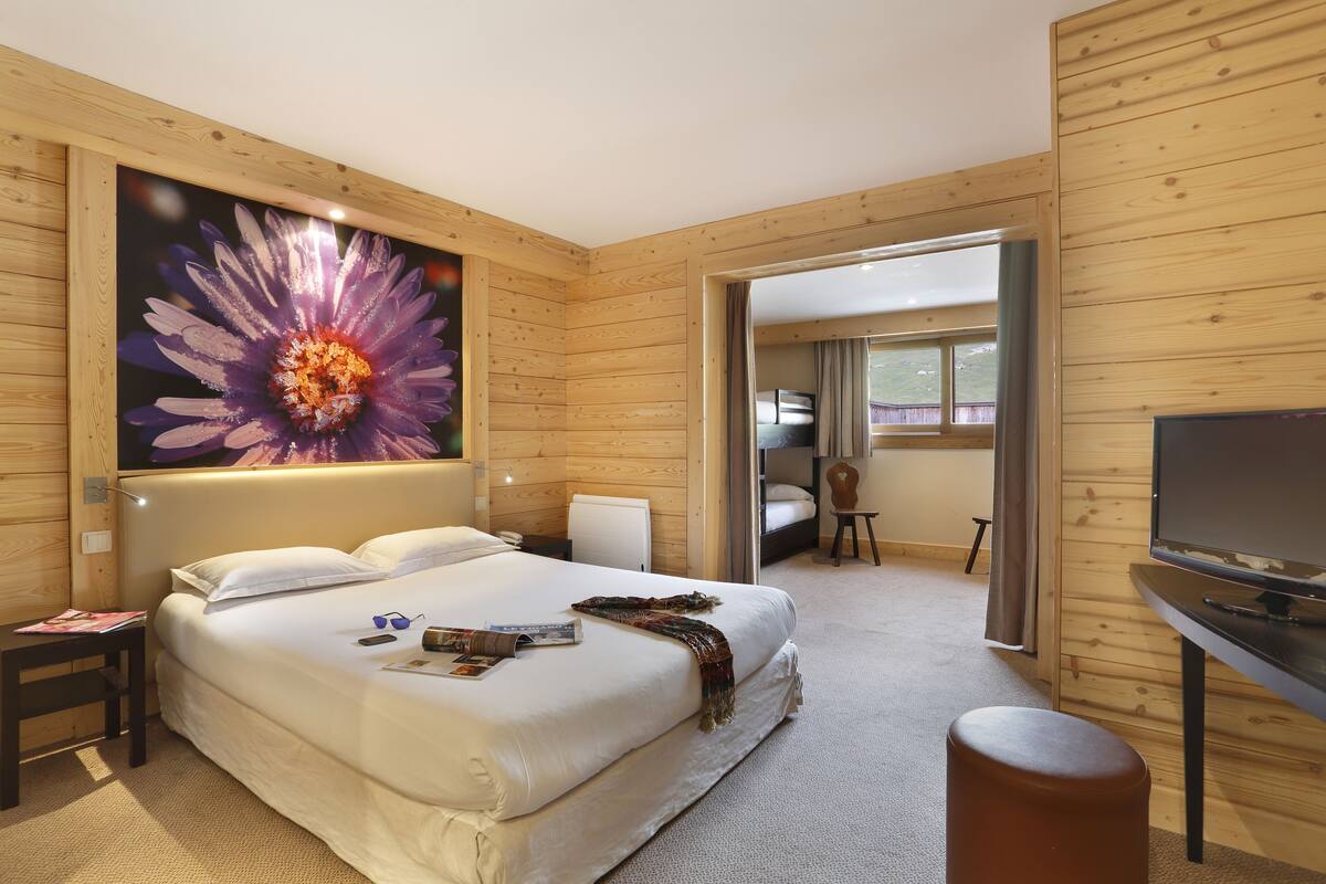Una habitació d'hotel amb un llit gran, una televisió, un escriptori i una porta que condueix a una altra habitació.