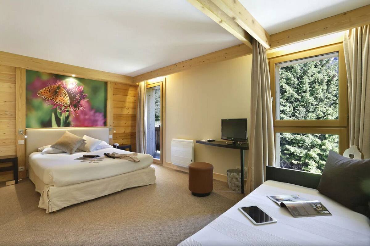 Habitació d'hotel amb un llit, una escriptori amb un ordinador, una finestra amb cortines i un quadre de flors a la paret.