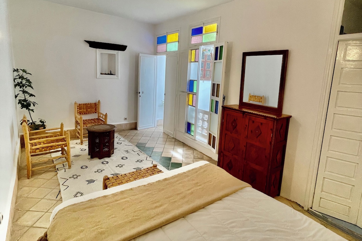 A bedroom with a bed, a wooden chair, a small table, a wardrobe, and a mirror.