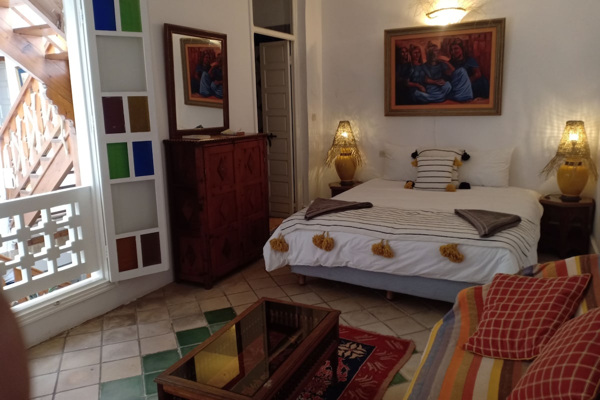 Une chambre à coucher comprenant un lit, deux lampes de chevet, une commode, un miroir et un mur orné d’un tableau encadré.