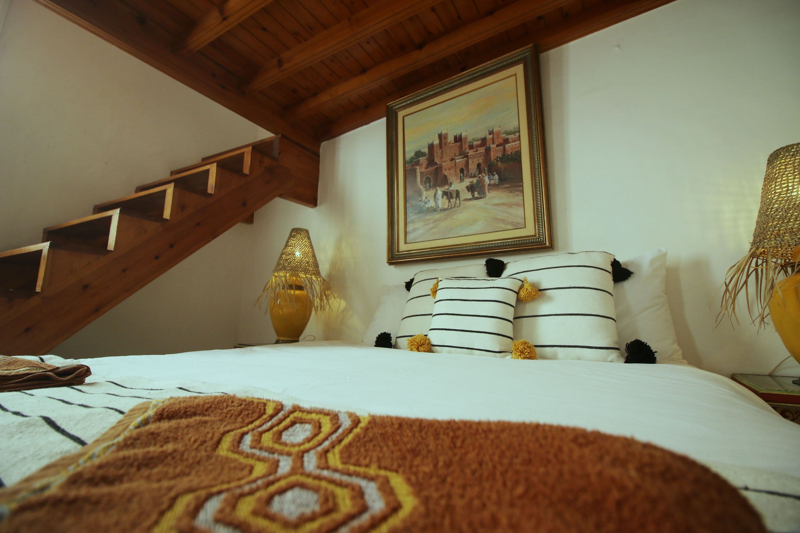 Un dormitorio con una cama, un cuadro, una lámpara y una escalera.