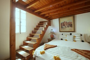 A bedroom with a wooden staircase, a bed with striped bedding, and a painting on the wall. - Darzayna (Essaouira)