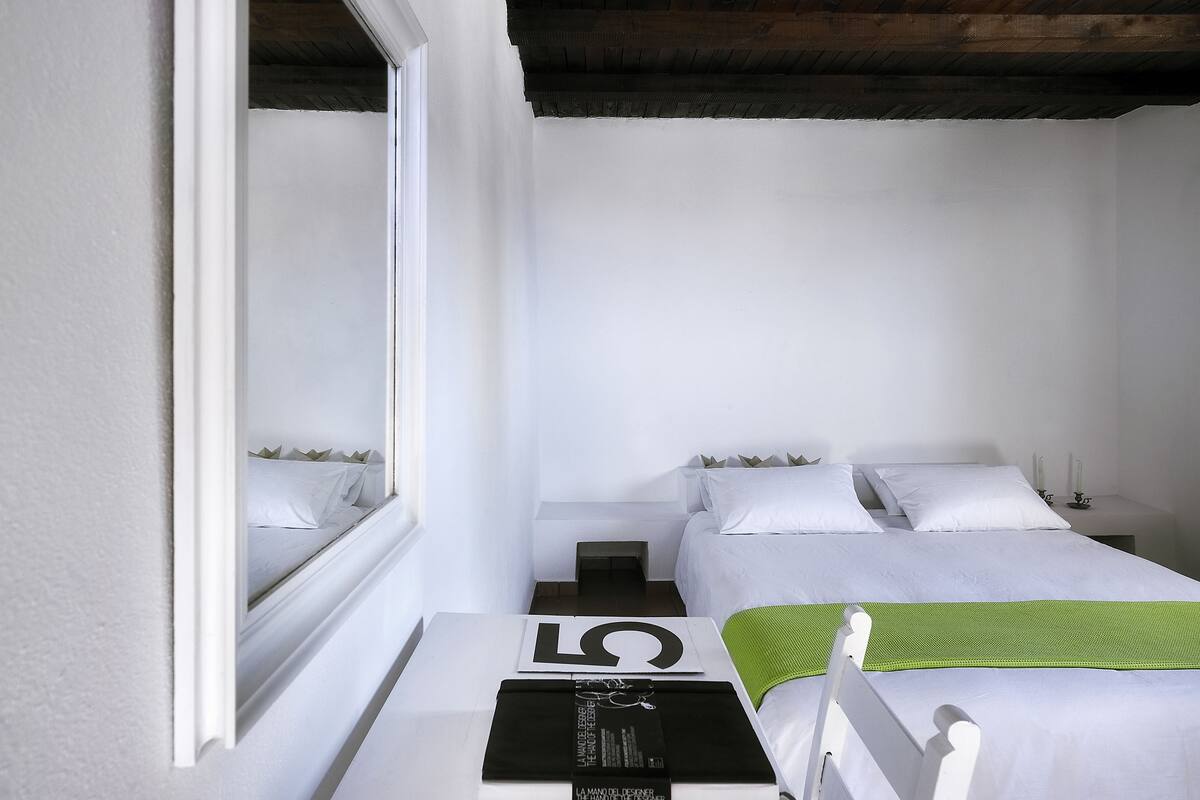 A minimalist bedroom with two beds, a large window, and a green throw on one bed.