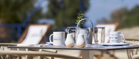 A table with a white mug, a white pitcher, and a white cup with a blue design, set on a table near a pool.
