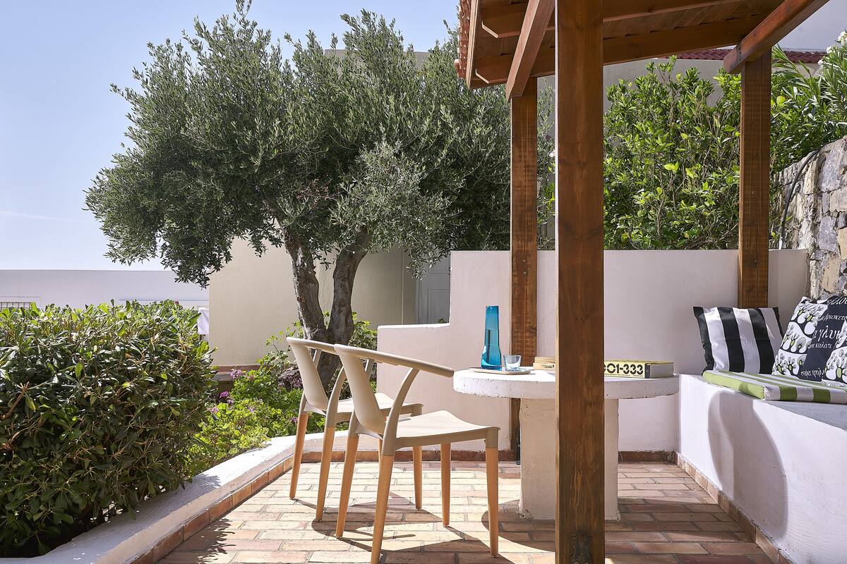 A patio area with a wooden pergola, a round table with two chairs, and a small seating area with cushions.