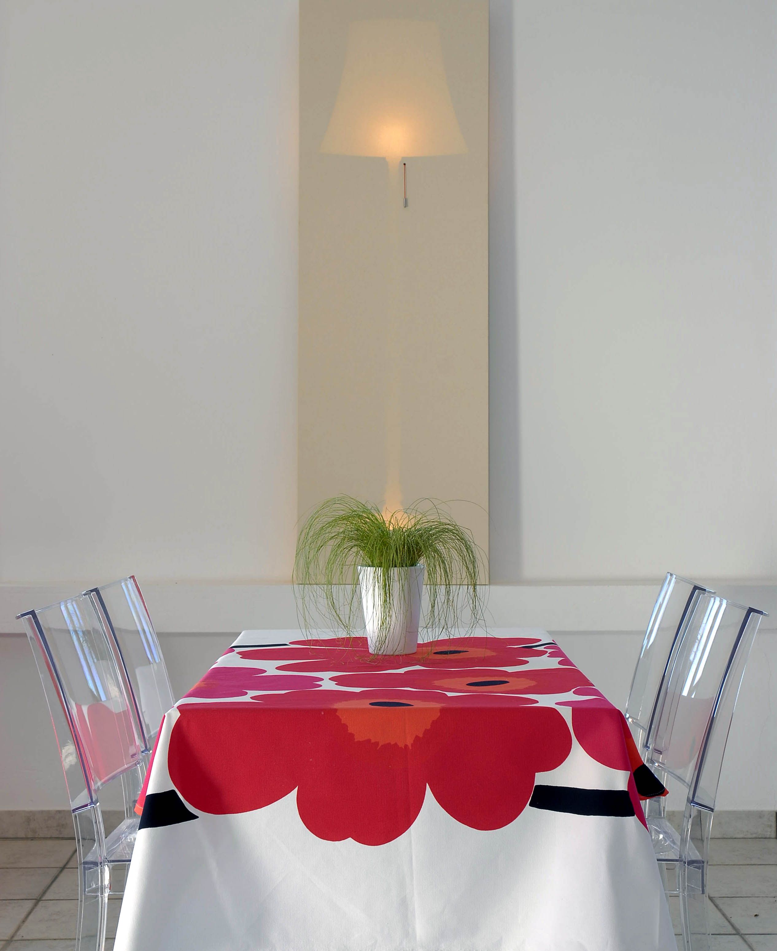 A dining table with a red and white tablecloth, clear chairs, and a potted plant in the center.