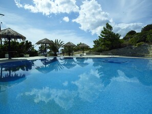 Una piscina con agua cristalina azul, rodeada de palmeras y sombrillas de paja.