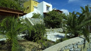 A two-story building with a yellow and white facade, surrounded by greenery and a stone wall. - Nakou Village (Ierapetra)