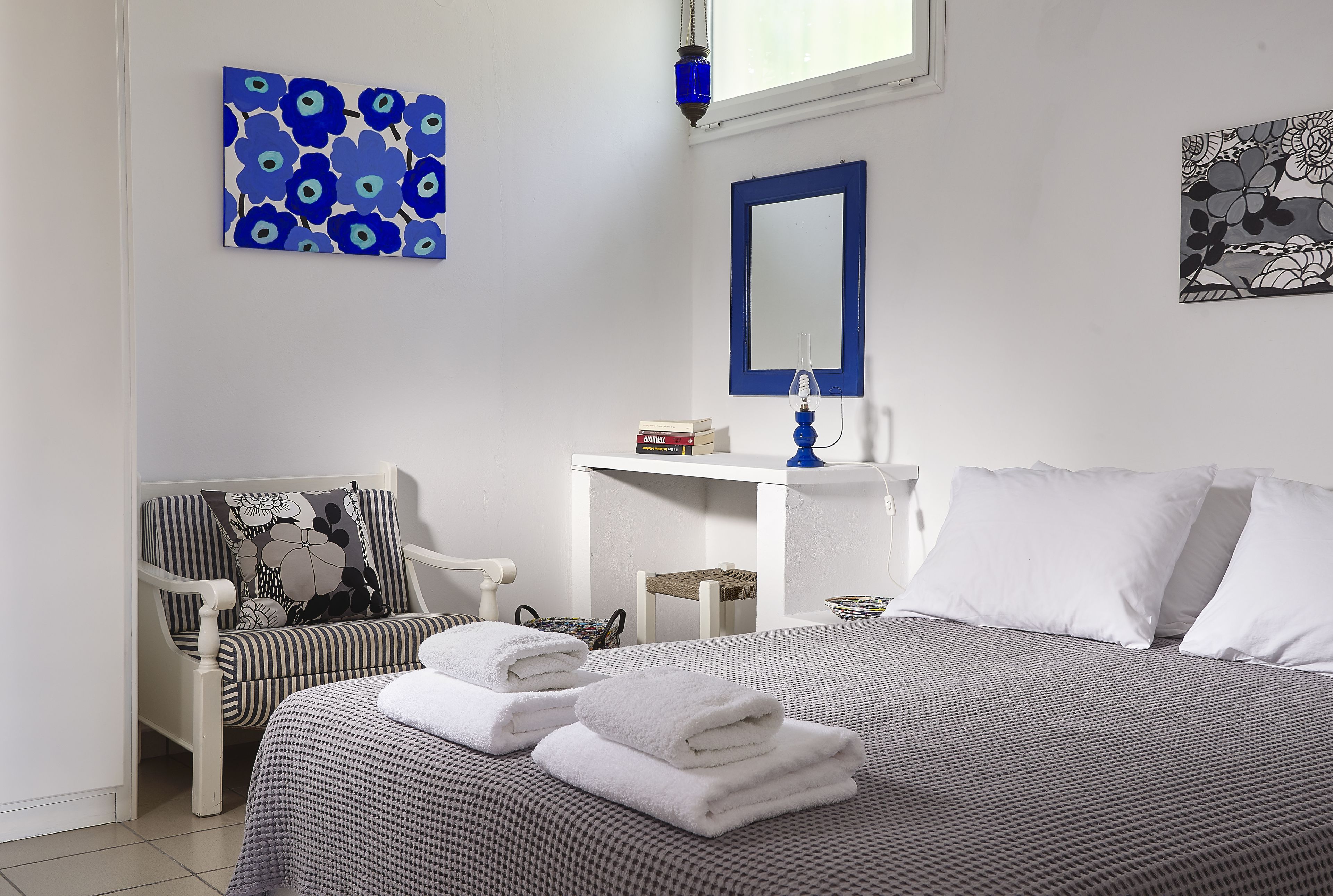 A neatly arranged bedroom with a bed, a chair, a bedside table, and a mirror.