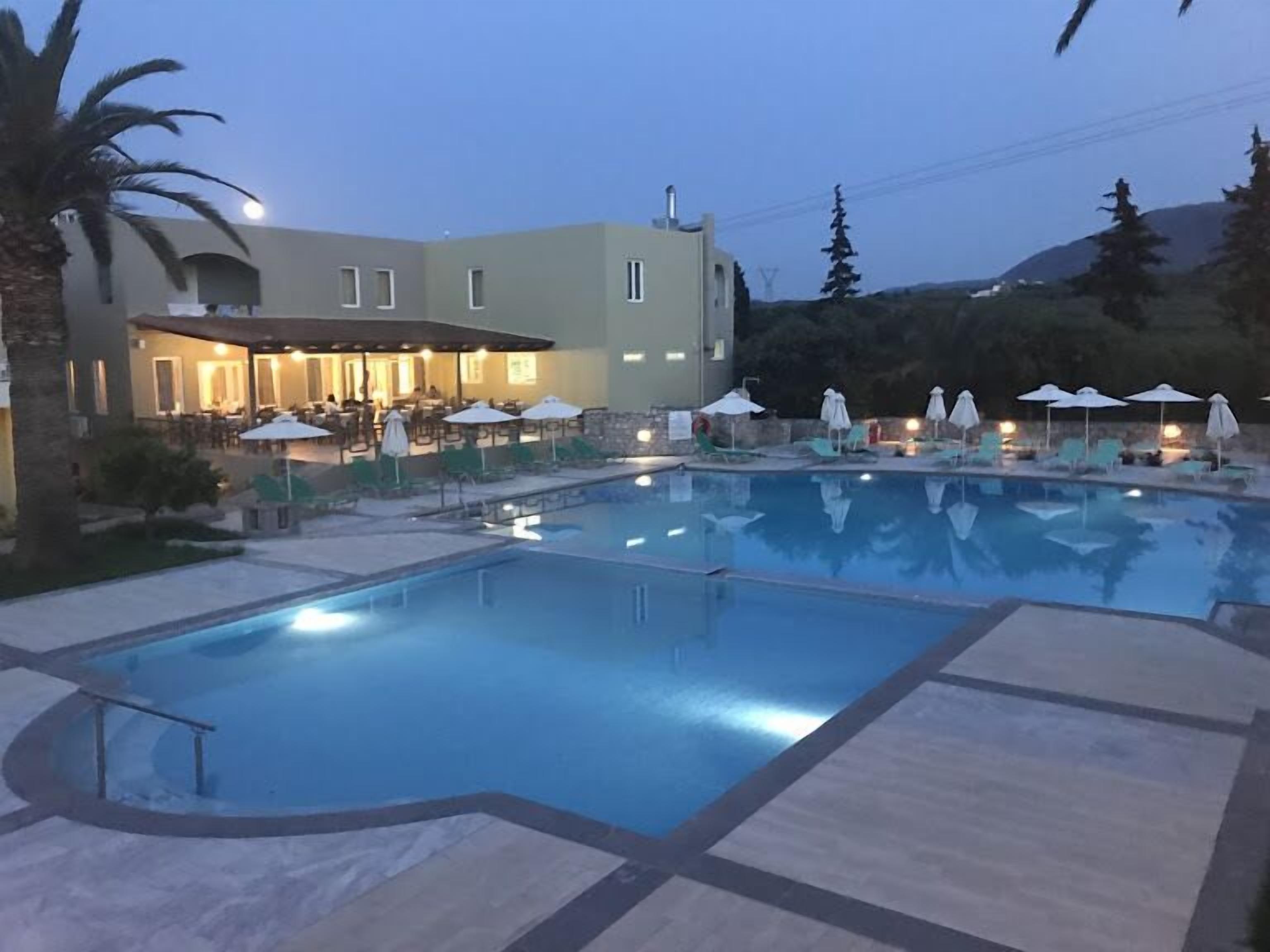 Un hotel con piscina, mobiliario de exterior y montañas al fondo.