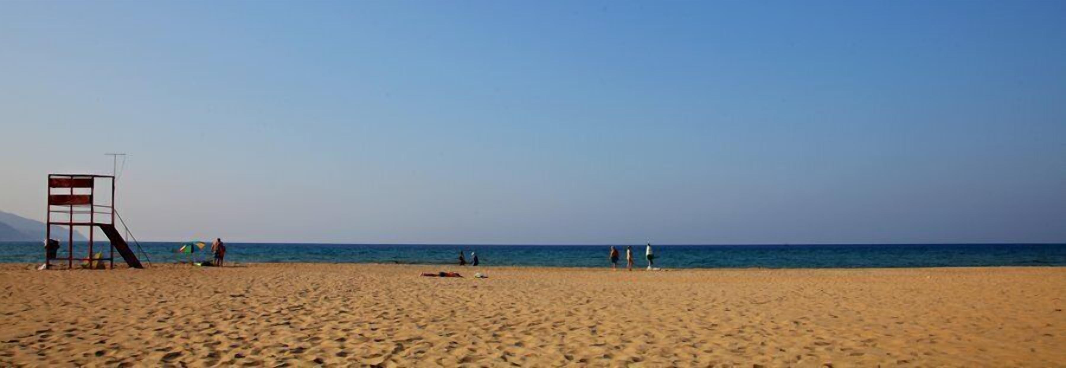 Una playa con una torre de salvavidas, cielo despejado y mar tranquilo.