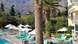 Ein Poolbereich mit Liegestühlen und Sonnenschirmen, Palmen und einem Bergpanorama.