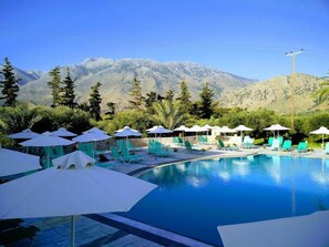A pool area with lounge chairs and umbrellas, surrounded by mountains. - Vardis Olive Garden (Apokoronas)