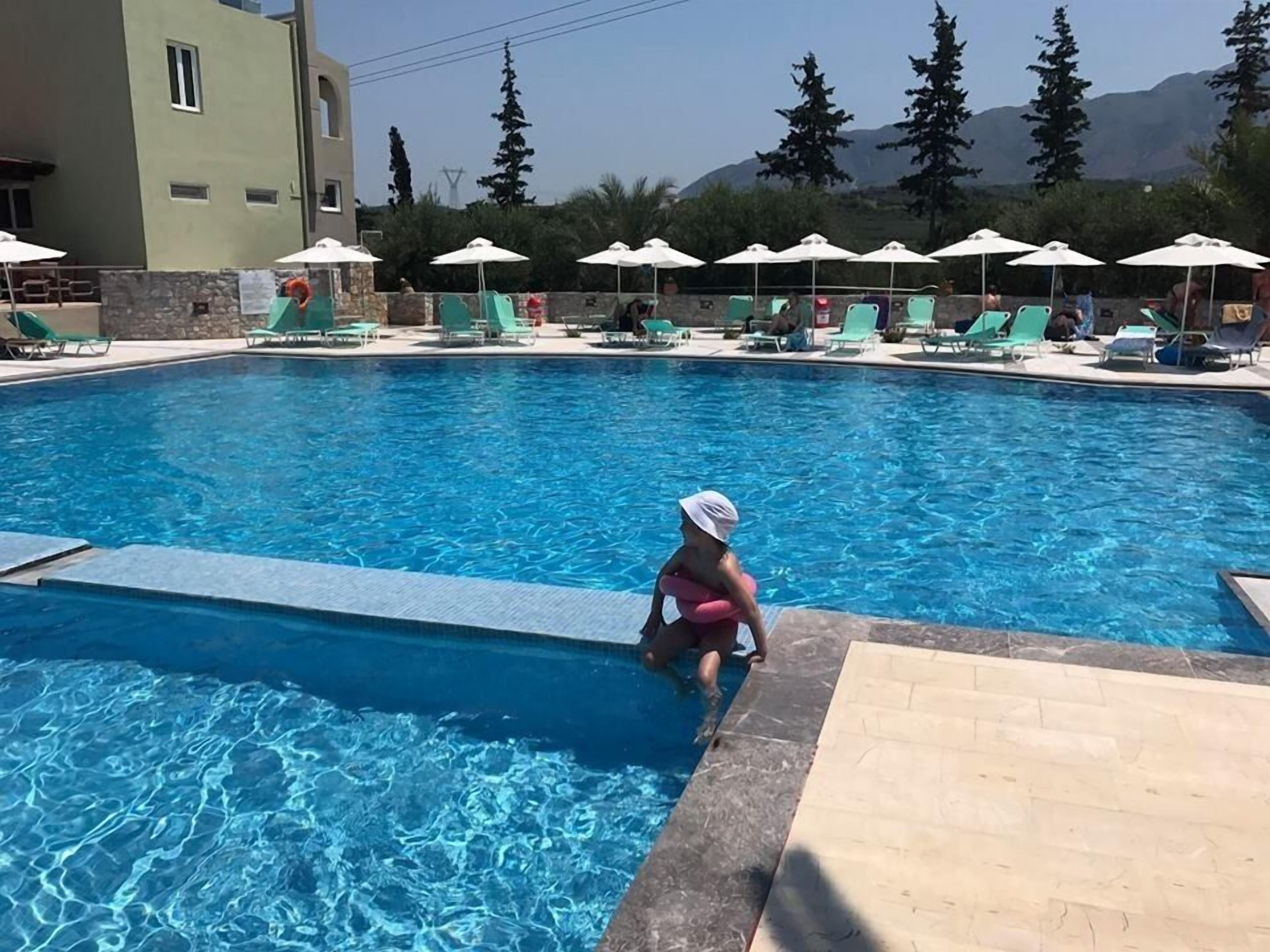 A swimming pool with lounge chairs and umbrellas, surrounded by a stone wall and trees.